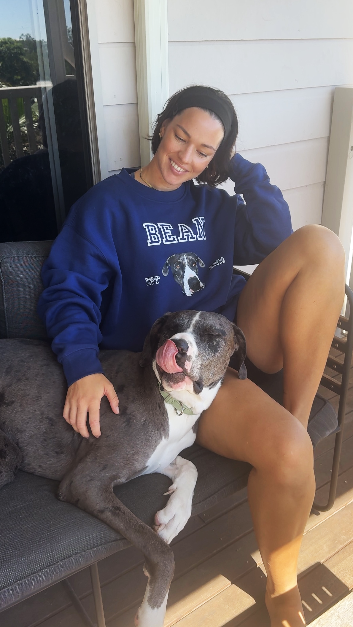 Woman in a blue sweatshirt sitting on a porch with a large dog.