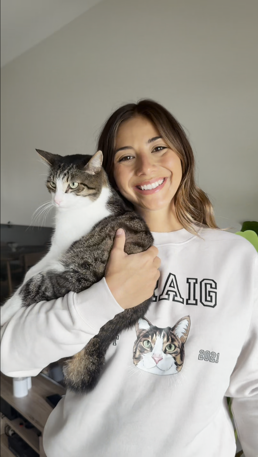 Woman holding a cat and wearing a sweatshirt with a cat design.