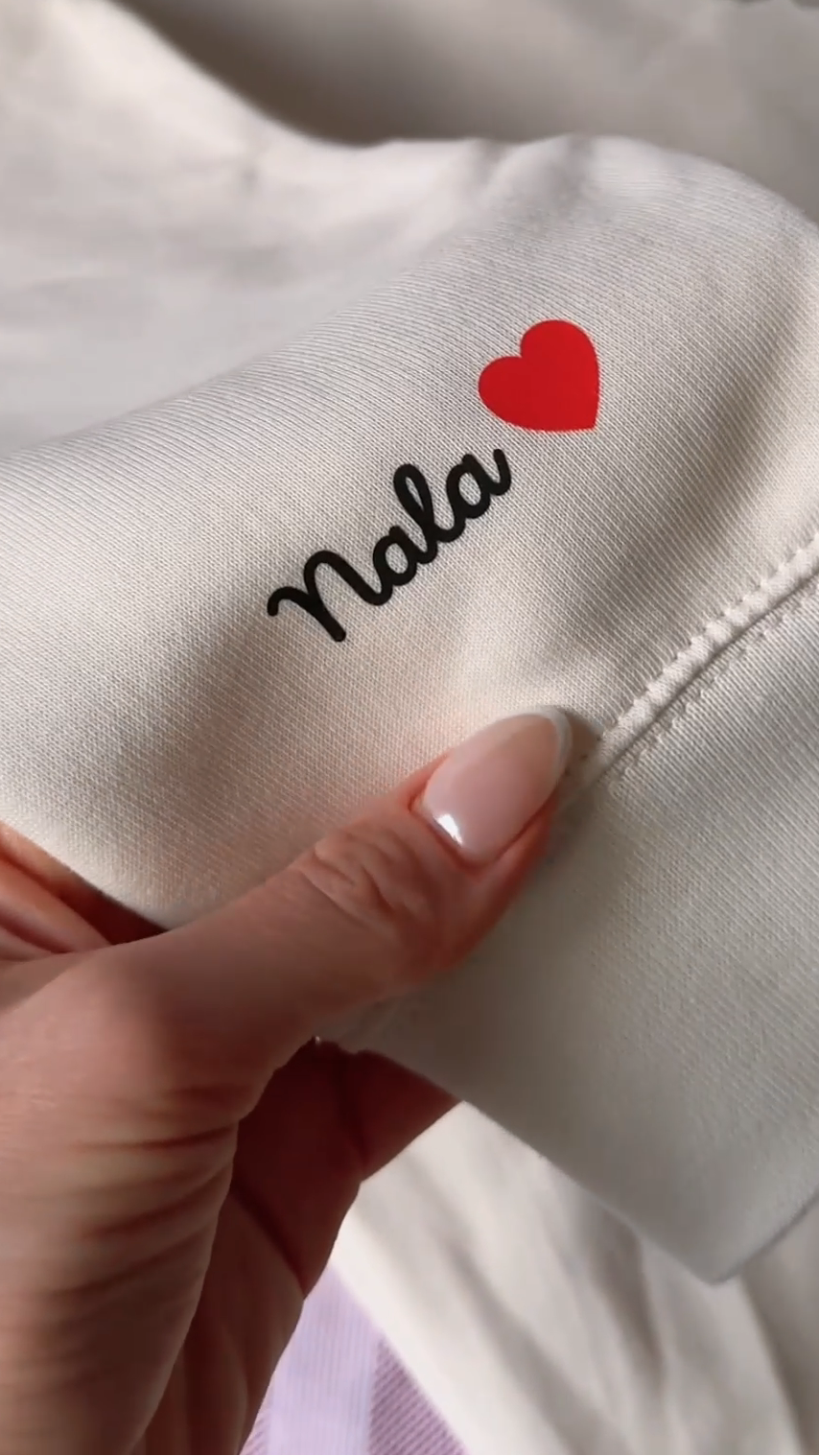 Text 'Nala' with a red heart on a white fabric held by a hand.