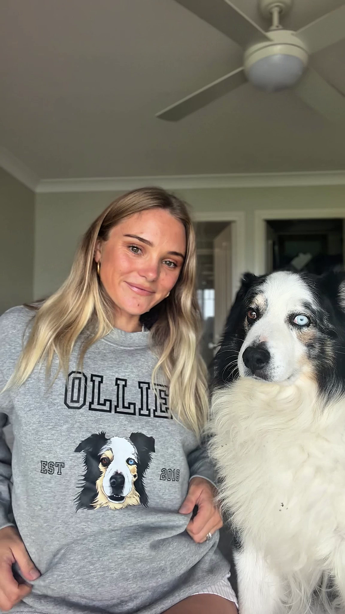 Woman wearing a gray sweatshirt with a dog's face and name, standing next to a black and white dog.